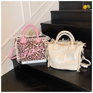 Detail of leopard print and solid canvas tote bags with fringe trim and logo lettering