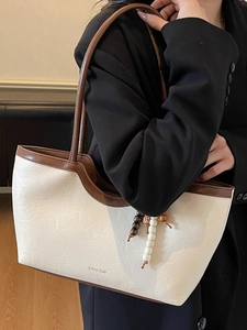 Sac cabas tissé crème avec bordure marron et perles porté par un mannequin en tailleur