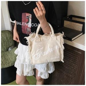 Detailed view of beige canvas tote bag with fashion fringe and casual text design