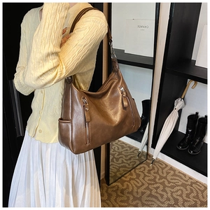Close-up of brown leather hobo bag with vintage texture and decorative metal zippers