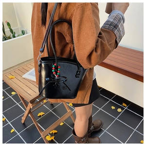 Detail shot of a black leather bucket bag with bow and beads in an autumn outdoor setting
