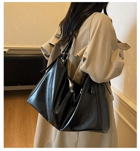 Modern black oversized hobo tote bag in glossy leather worn with a beige trench coat