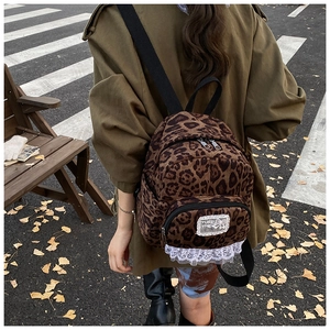 Detail view of leopard print backpack with white lace trim and chic woven patch on street