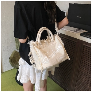 Detail of canvas tote bag with fringe edges, fashion text print, and round handles