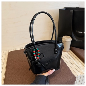 Detail of a black glossy bucket bag featuring a decorative beaded charm with red and green accents