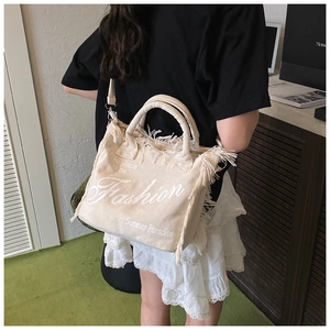 Detailed view of beige canvas tote with fringe trim and shoulder strap on model