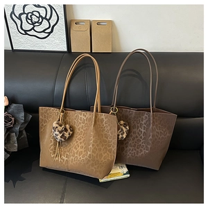 Detail view of large leopard print tote bags with heart plush charms on a black sofa