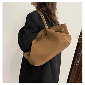 Detailed close-up of brown suede tote bag featuring embossed textures and metal buckles