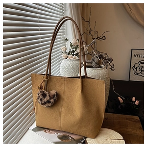 Detail of tan suede tote bag with leopard heart charm on a sunlit wooden table