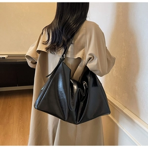 Detail view of large black glossy leather tote bag showing slouchy texture on model shoulder