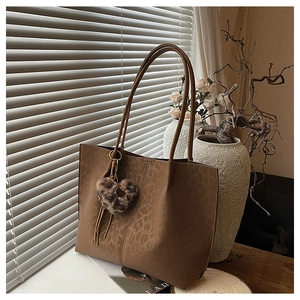 Close-up of leopard embossed brown tote bag with plush heart charm and tassel detail