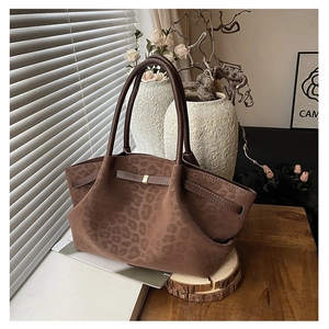 Detail of large brown leopard print suede tote bag with metal buckles on a wooden table