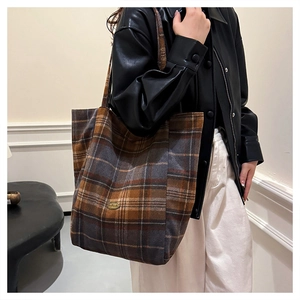 Detail of checkered tote bag with gold metal plaque shown on black leather jacket