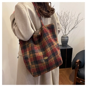 Close-up of vintage red plaid tote bag featuring a gold metal emblem and wide strap