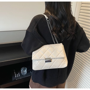 Close-up of cream quilted chain bag with silver buckle worn on a model's shoulder
