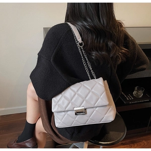 Rear view of a model wearing a grey quilted crossbody bag with silver chain and lock