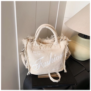 Detailed close-up of cream canvas tote bag featuring decorative fringe and fashion print