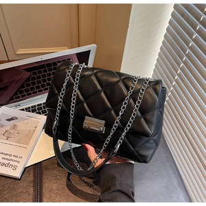 Close-up of black quilted shoulder bag with silver chain strap and metal turn-lock clasp