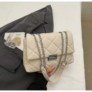 Close-up of beige quilted chain bag with silver buckle on a gray blazer background