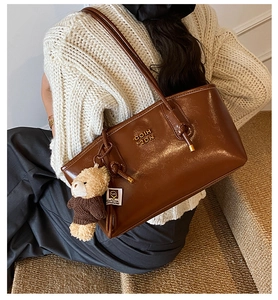 Detail of a brown leather tote bag with gold lettering and a cute teddy bear charm