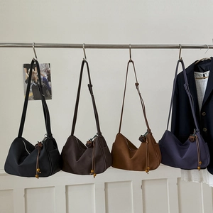 Row of minimalist suede shoulder bags in black, brown, and navy with tassel details