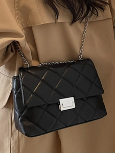 Classic black quilted crossbody bag with silver chain strap on khaki trench coat