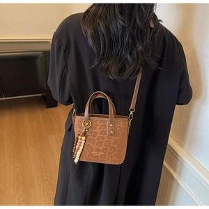 Detail of a brown leopard print bucket bag with beaded charm on a black blazer