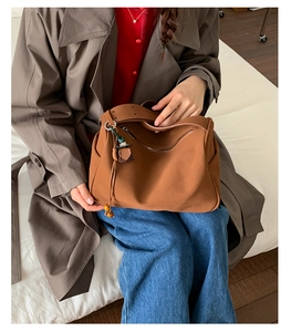 Detail of a brown faux suede tote bag with a metal zipper and wooden bead tassel