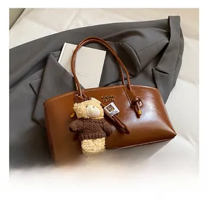 Detail of vintage brown shoulder bag with metal logo and cute plush bear charm decoration