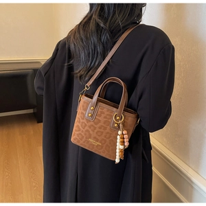 Detail of a brown leopard print crossbody bag with velvet texture and beaded tassel charm
