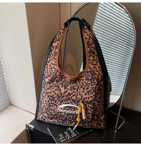Détail du sac hobo léopard avec pendentif à franges et poche avant sous une lumière chaude