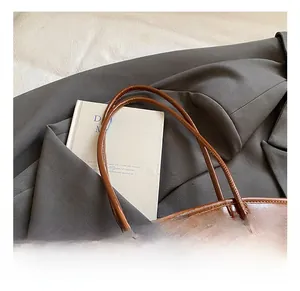 Detailed macro view of smooth dark brown leather straps and gold metal logo on the tote bag