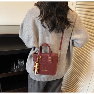 Detail of burgundy leopard embossed bucket bag with wooden bead charm on a model