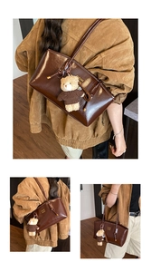 Brown leather tote bag featuring brand lettering and cute teddy bear pendant charm