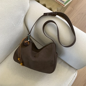 Detail of dark brown faux suede hobo bag with tassel wood bead charm on a sofa