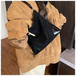 Detail of black faux suede crossbody bag with asymmetric design and beaded pendant accessory