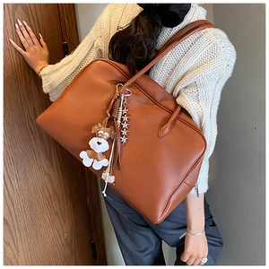Detail of brown lychee-grain tote bag featuring a cute white schnauzer charm and star pendant