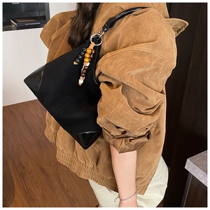 Detail of black geometric shoulder bag featuring suede texture and wooden bead tassel