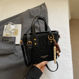 Detail of black leopard embossed tote bag with gold ring and wooden bead tassel