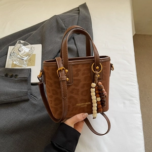 Detail of leopard print handbag featuring wooden bead charm and brown leather trim
