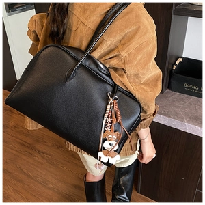 Detail of black pebbled leather tote bag with a unique schnauzer charm and shoulder strap