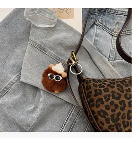 Detail eines braunen Plüschball-Anhängers mit weißer Strickmütze und Sonnenbrille an der Tasche