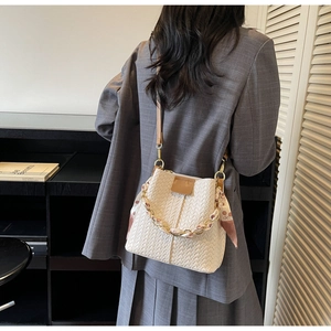 Detail of a beige woven bucket bag featuring a silk-wrapped chain handle and leather strap