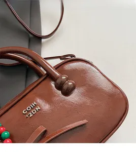Detail of brown oil wax leather pillow bag with embossed lettering and beaded charm
