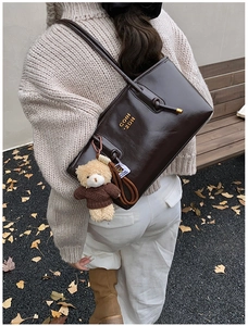Detail of dark brown glossy leather shoulder bag with cute teddy bear bag charm