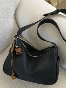 Minimalist black suede hobo shoulder bag with wooden bead charm on a beige sofa
