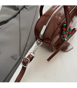 Detail of dark brown polished leather bag with silver zipper and beaded charm accent