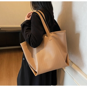 Detail view of a large brown crocodile pattern tote bag shown over the shoulder