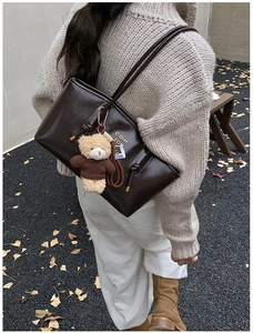 Detail of vintage brown leather tote bag with cute plush bear charm on a female model