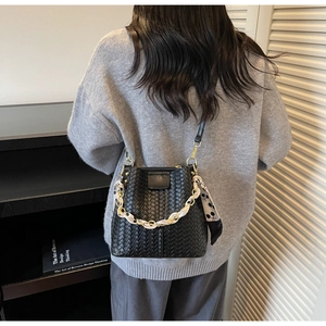 Detail of black woven bucket bag with metal chain handle and decorative silk scarf